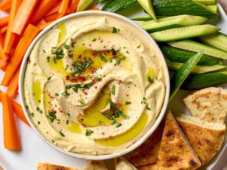 A plate of hummus with vegetables and bread nearby