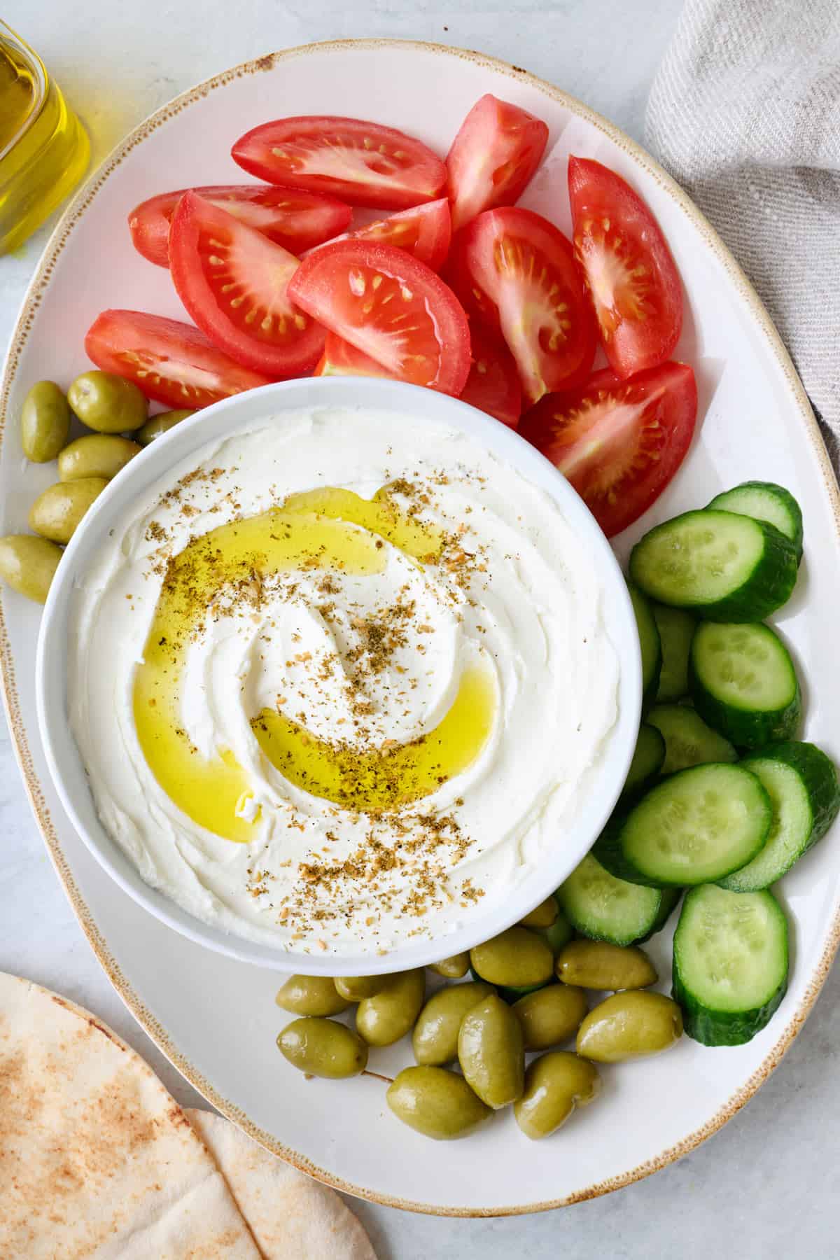 A plate of labneh with vegetables and bread around it